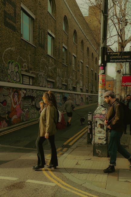A woman in a beige jacket and dark pants holds a bouquet of fresh flowers wrapped in light-colored paper, standing on a busy street corner in Spitalfields Market area. The bouquet features a vibrant m