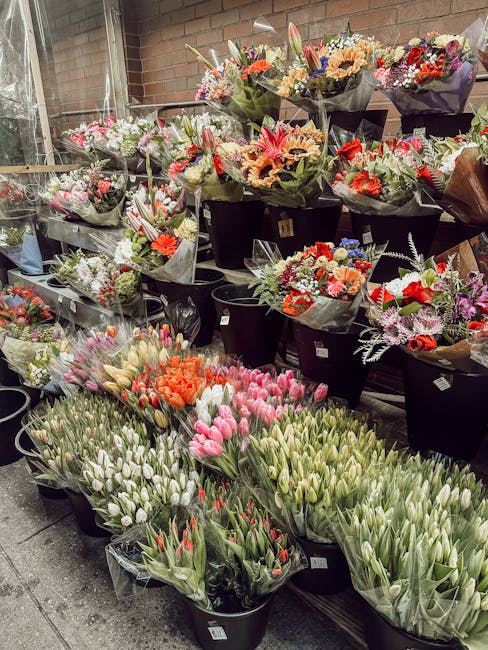 A display of freshly arranged floral bouquets and bunches of tulips at a flower shop. The bouquets feature a variety of colorful flowers, including pink, orange, red, and purple blossoms, wrapped in d